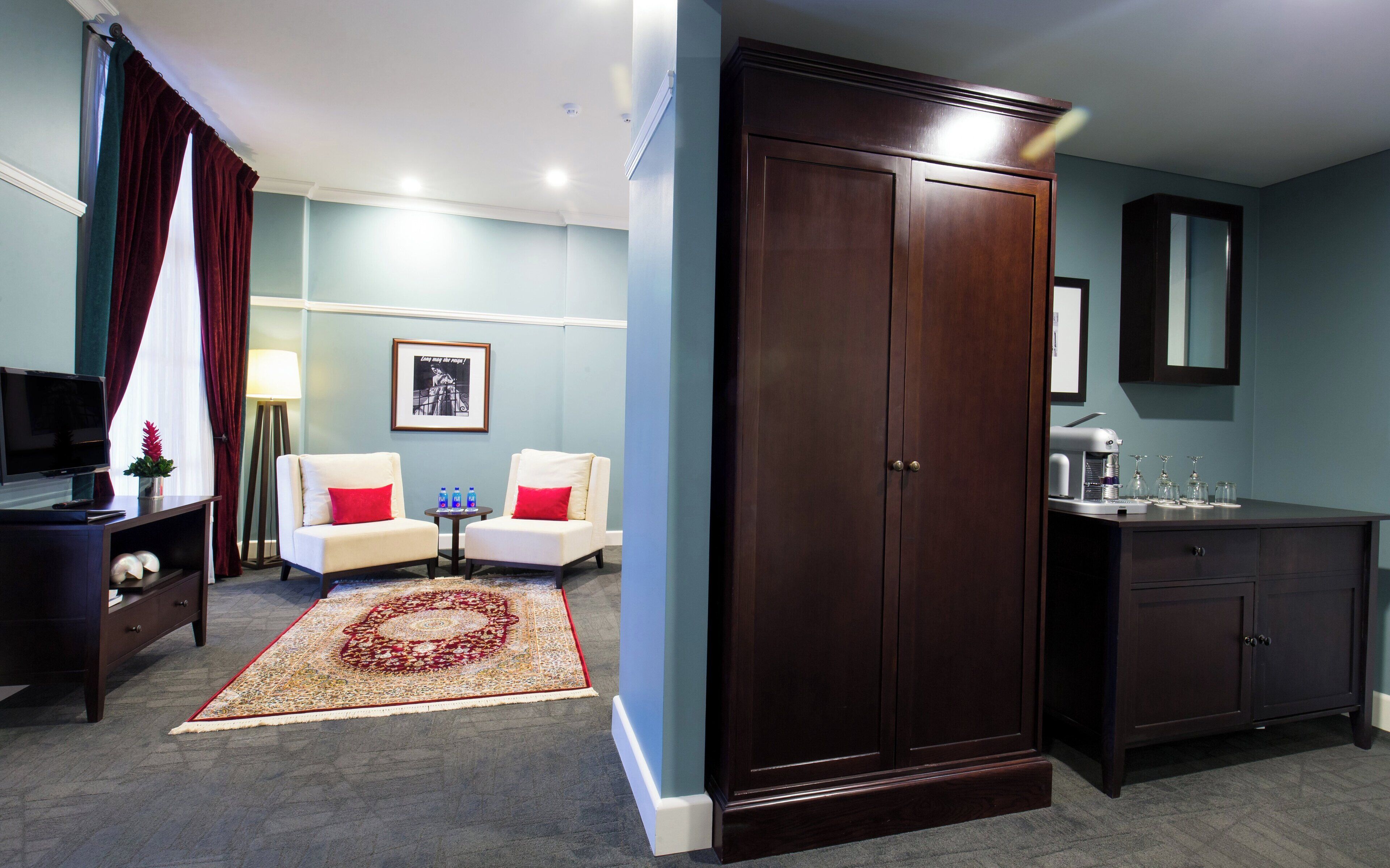 Habitación de hotel con un armario grande, dos sillones, una mesita de centro, televisor y baño con lavabo y espejo.