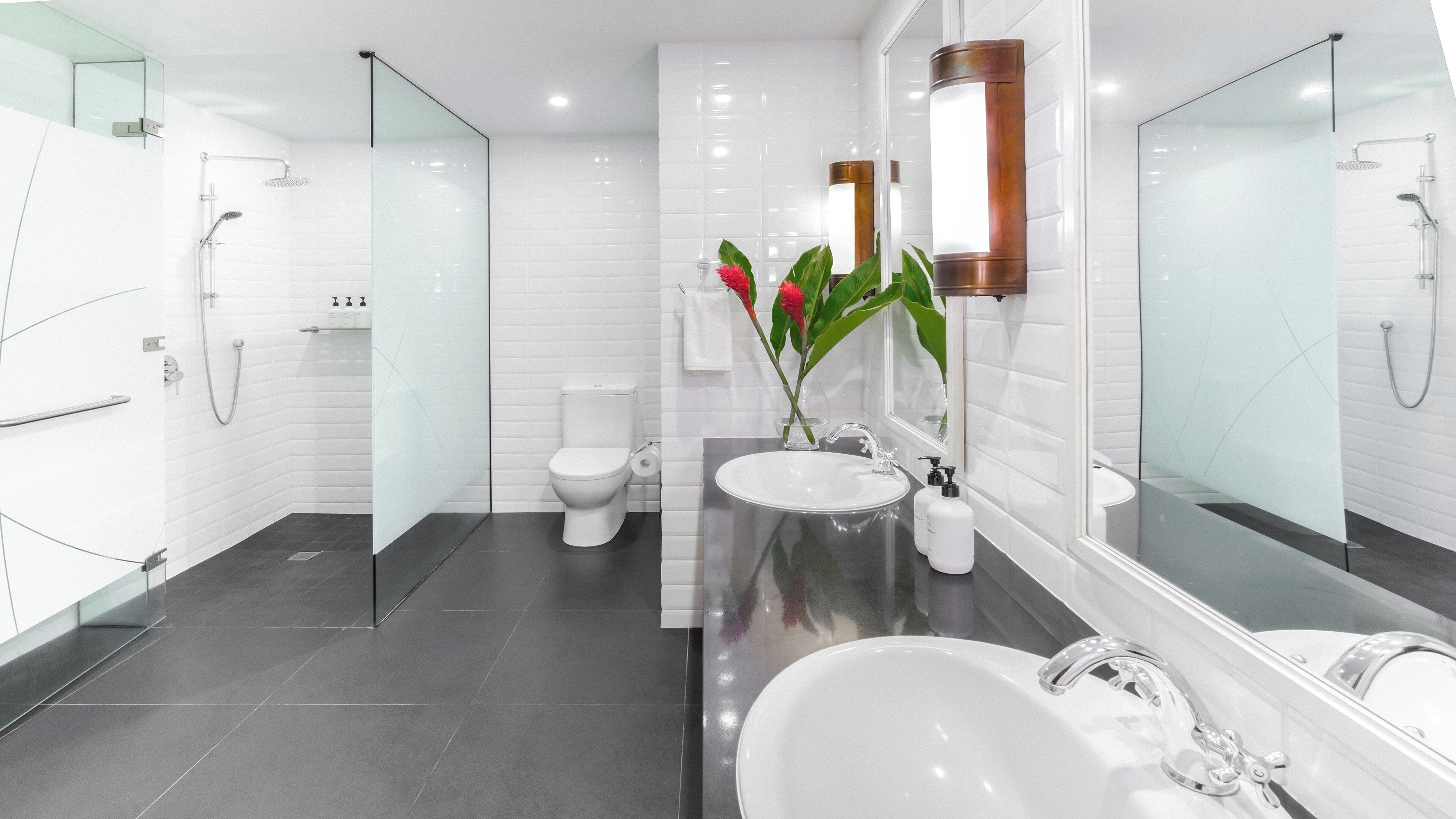 A modern bathroom with a glass shower enclosure, a white toilet, a large sink with a mirror, and a potted plant.
