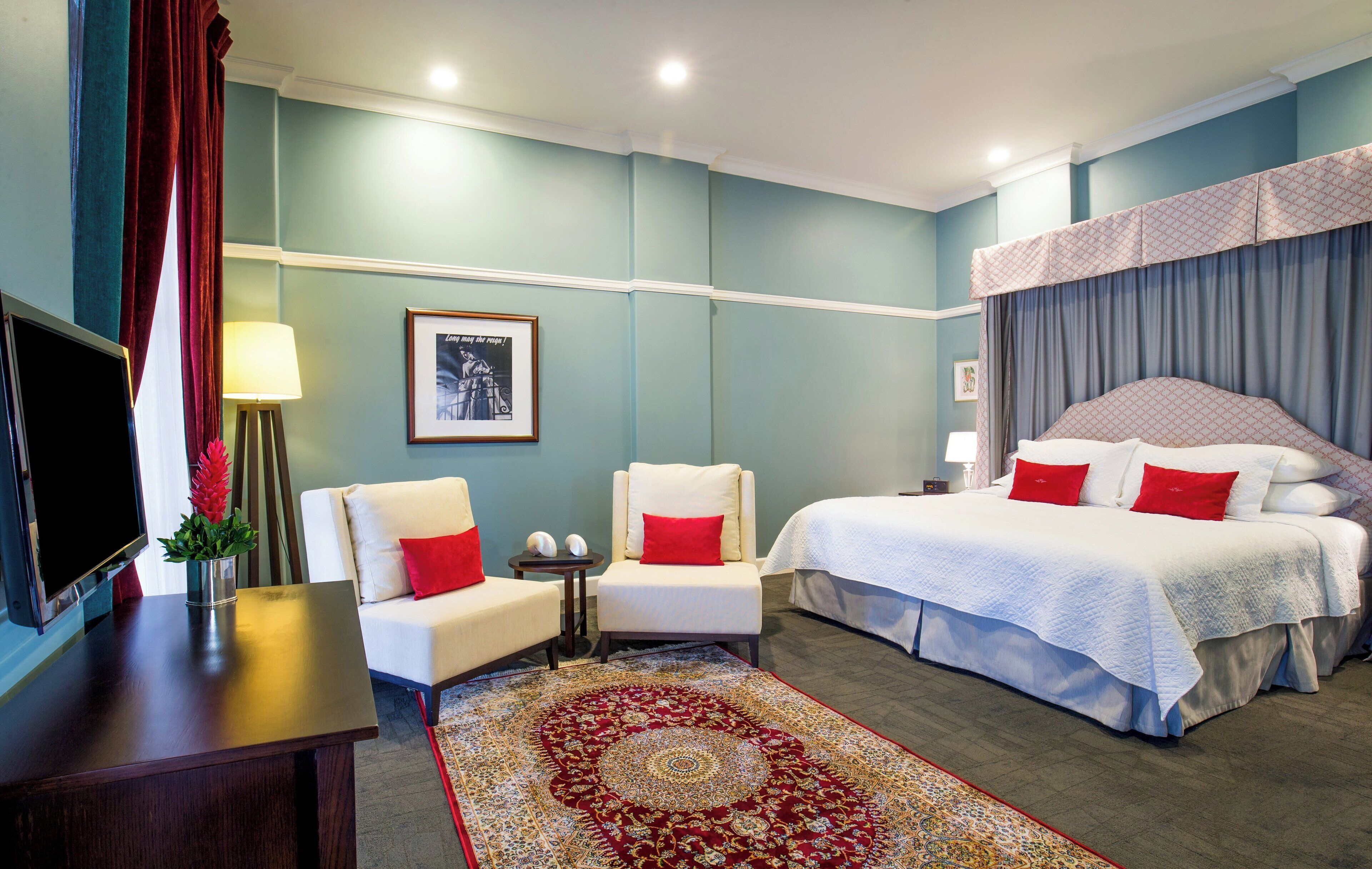 A hotel room with a bed, two chairs, a TV, a lamp, and a rug.