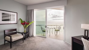 A hotel room with a balcony, a chair, a table, and a vase with flowers. - Grand Pacific Hotel Fiji (Suva)
