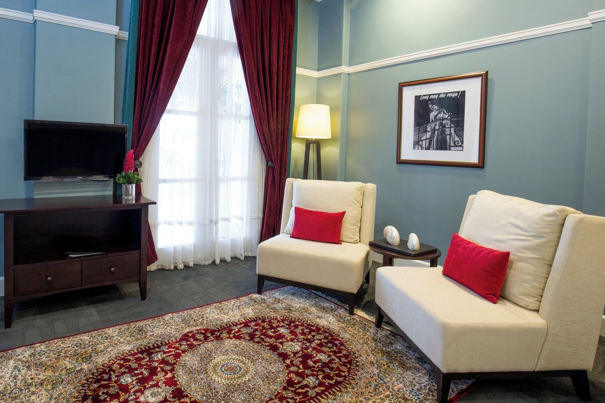 A living room with a television, two armchairs with red cushions, a lamp, and a framed picture on the wall.