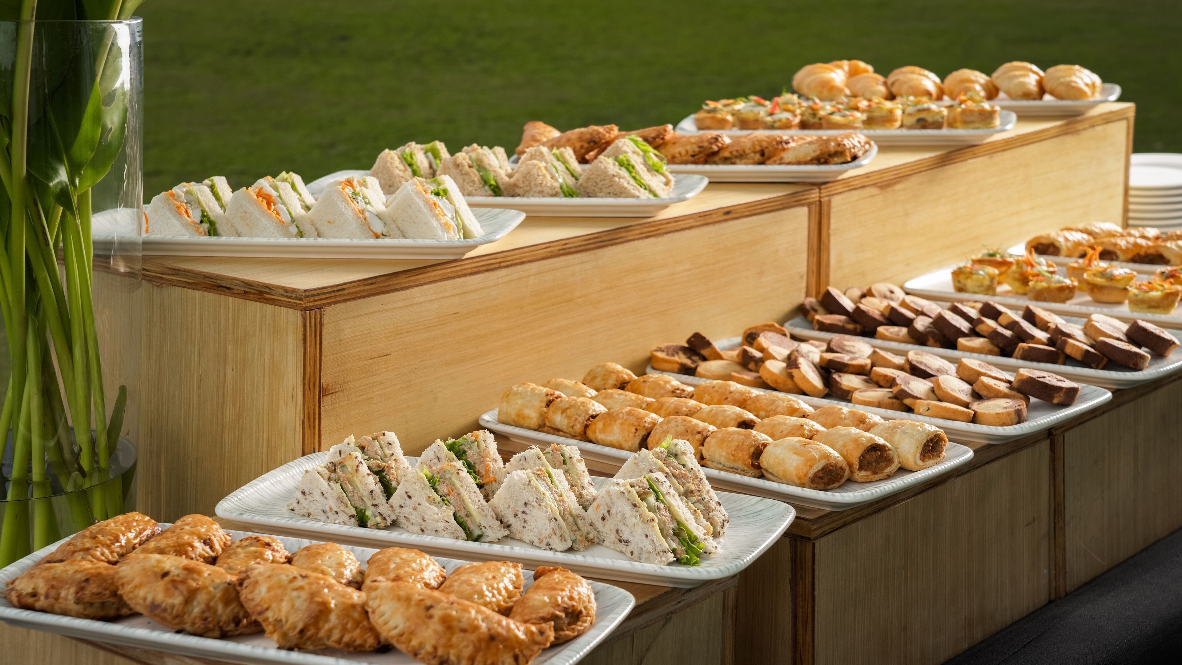 Un bufé con diferentes opciones de comida, incluyendo sándwiches, pasteles y postres.
