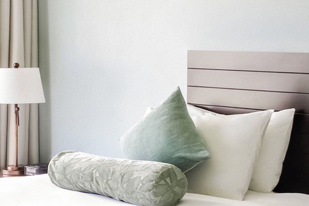 A neatly made bed with a pillow, a bedside lamp, and a headboard.