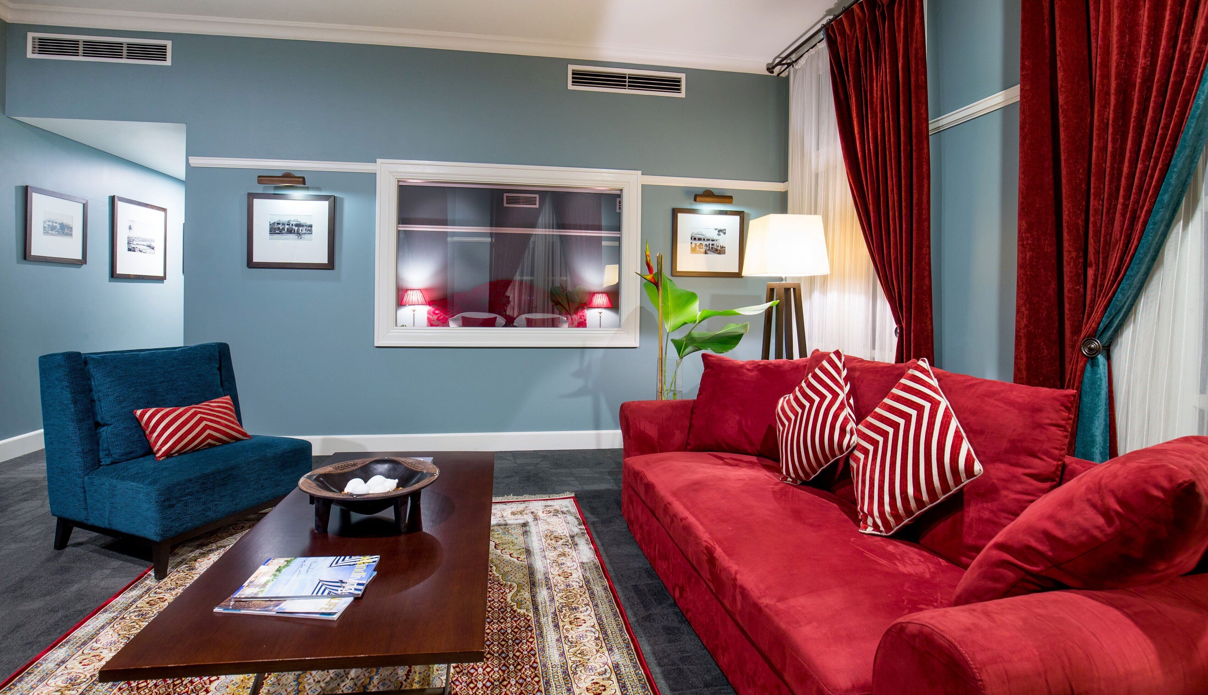 Una sala de estar con un sillón azul, un sofá rojo, una mesa de centro y cuadros en la pared.