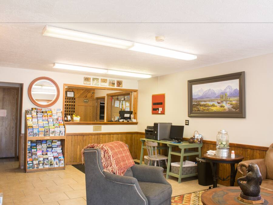 A reception area with a wooden desk, a computer, a chair, a bookshelf, and a framed landscape painting.