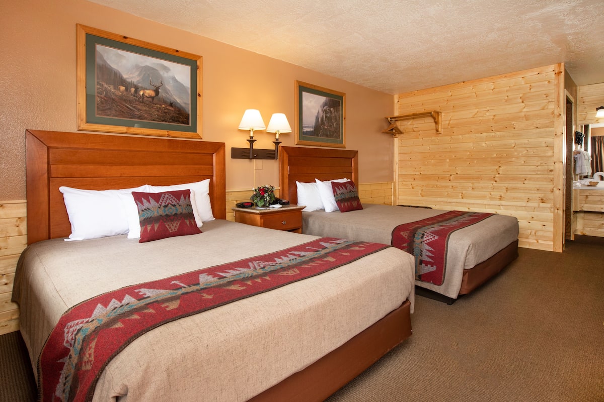Une chambre d’hôtel avec deux lits, des têtes de lit en bois, une table de chevet avec des lampes et des tableaux encadrés au mur.