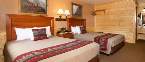 A hotel room with two beds, wooden headboards, a nightstand with lamps, and framed pictures on the wall.