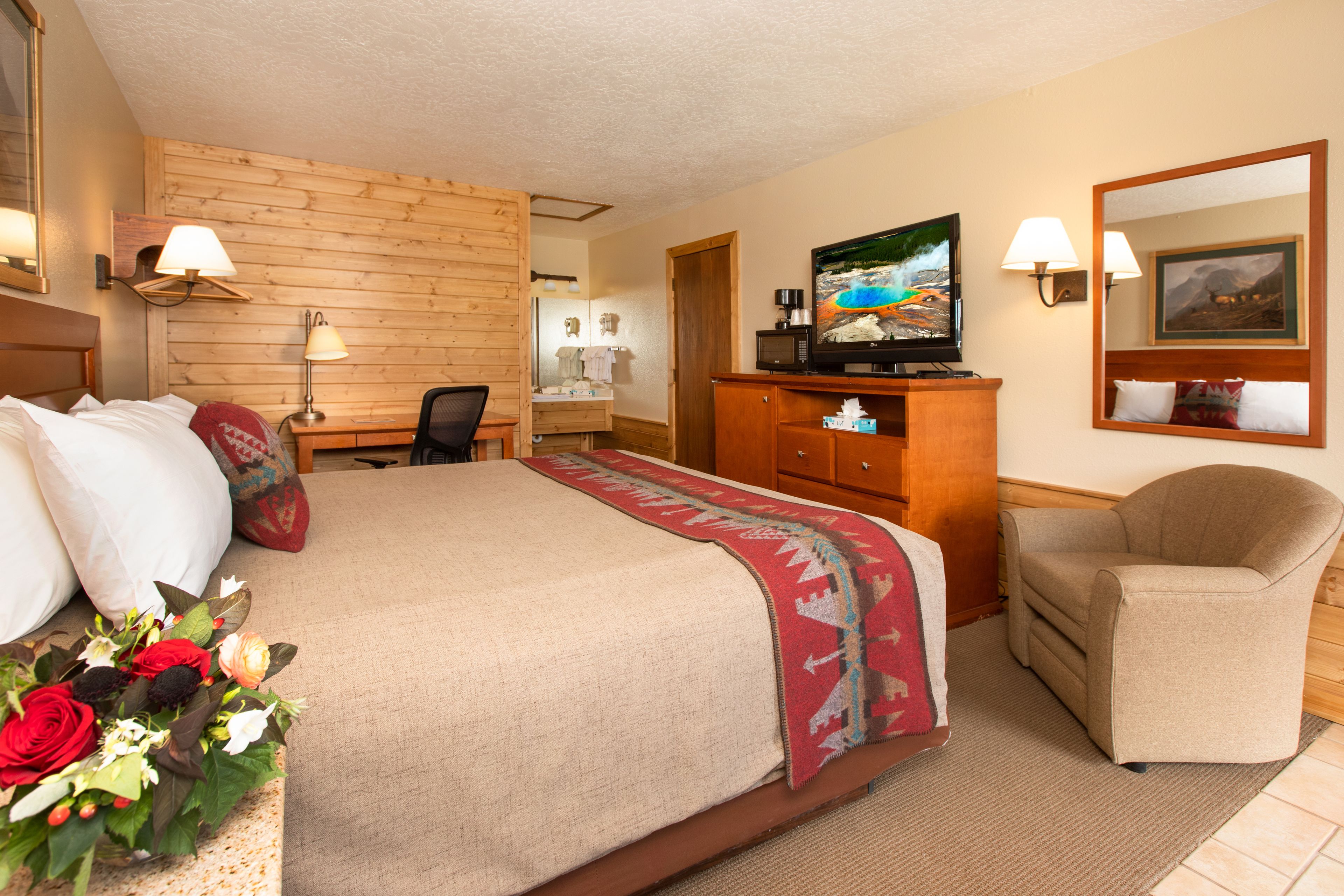 A hotel room with a bed, a desk, a television, a chair, and a mirror.