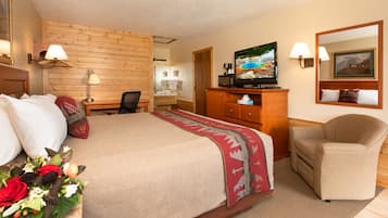Quarto de hotel com cama, escrivaninha, televisão, cadeira e espelho.