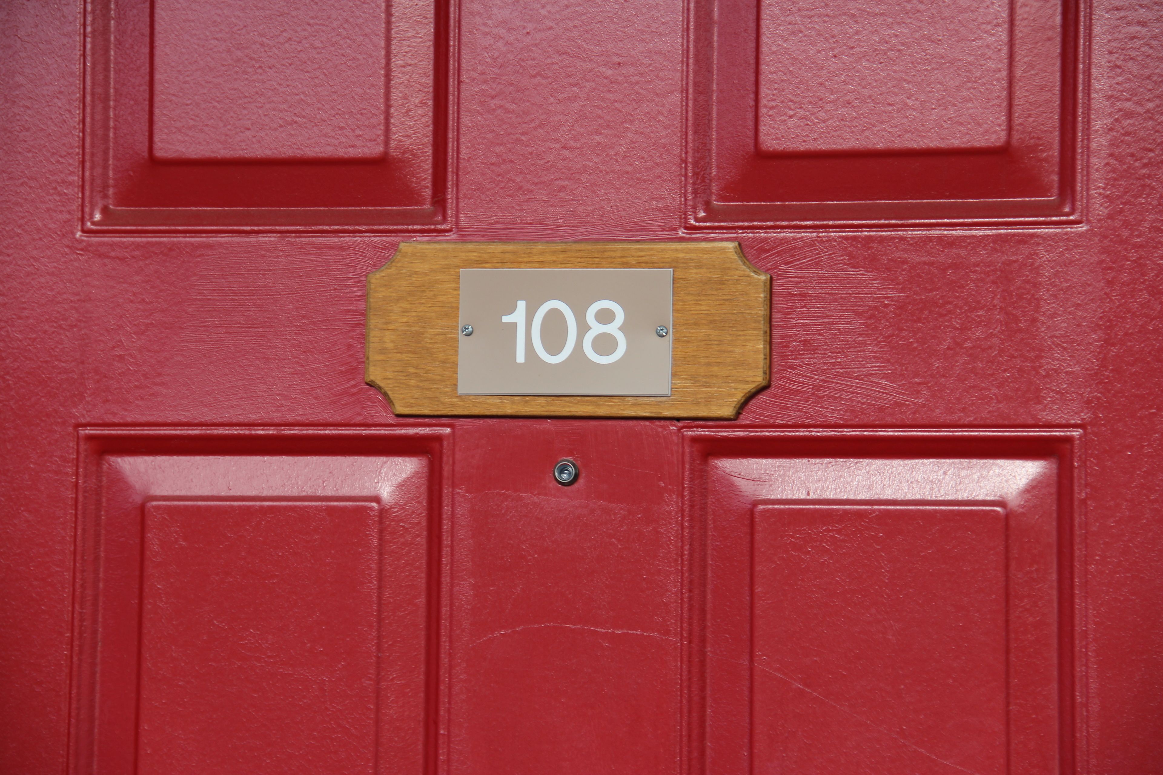 A red door with a wooden plaque displaying the number 108.