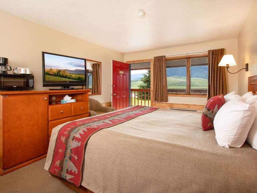A hotel room with a bed, a television, a desk with a microwave, and a view of the outdoors.