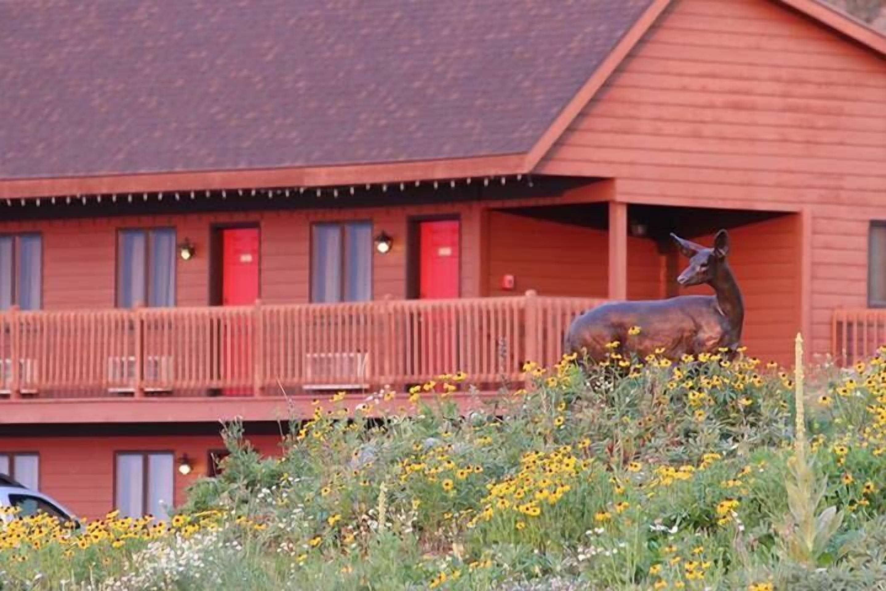 A rustic building with a red exterior, a balcony with a railing, and a deer statue in the foreground.