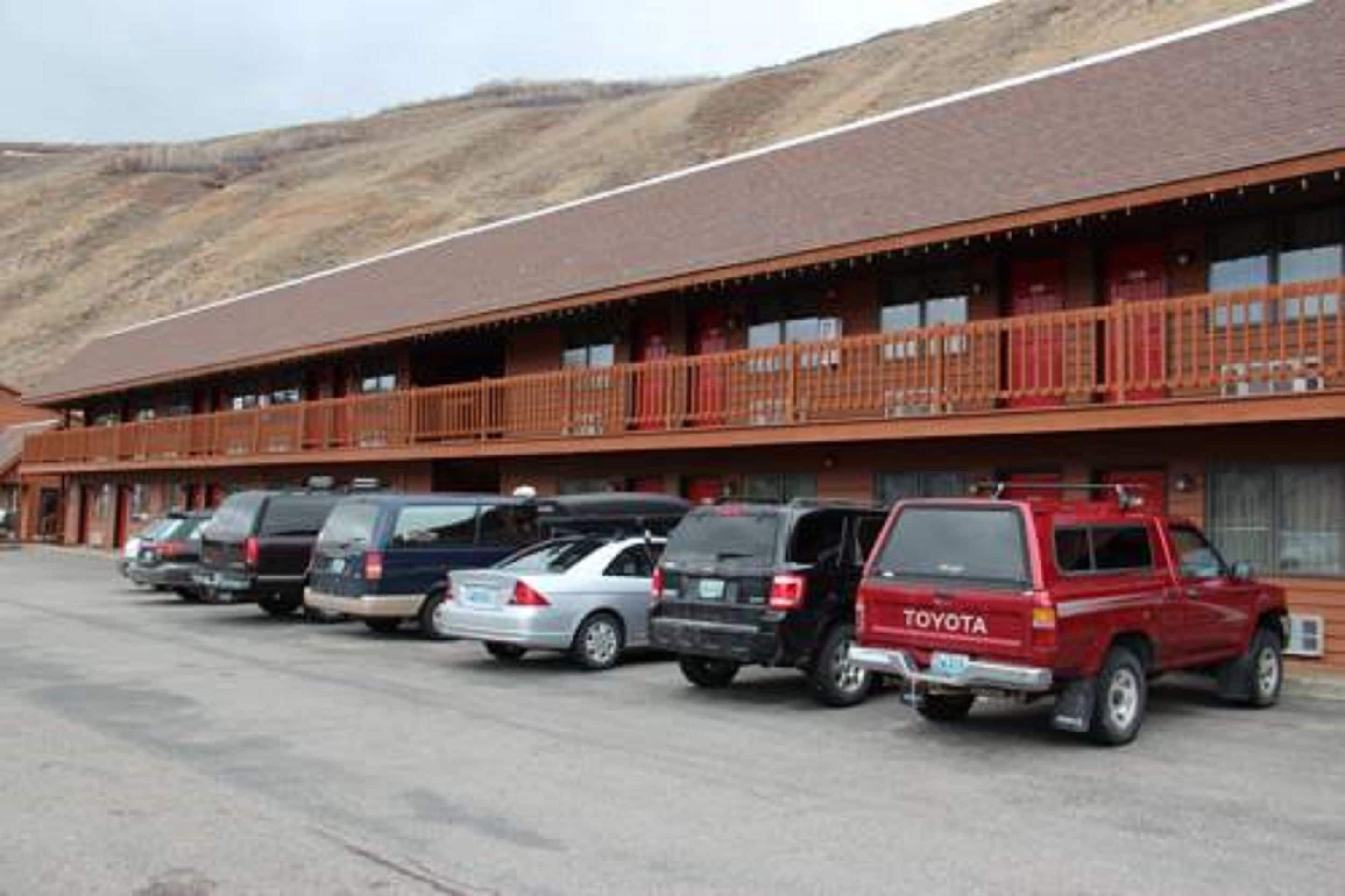 A motel with a row of parked cars in front, a red Toyota SUV, and a building with a red roof and balconies.