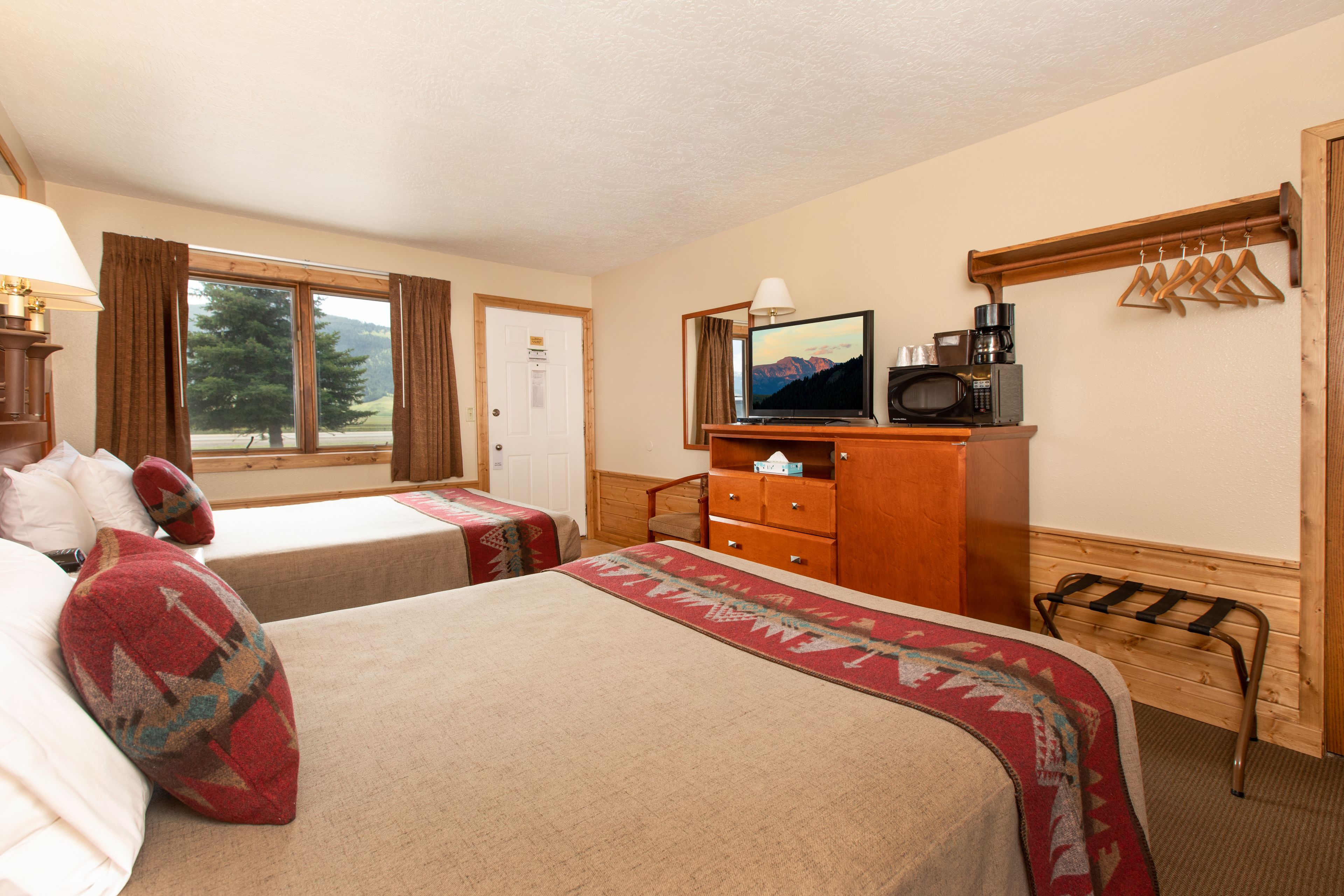 A hotel room with two beds, a television, a microwave, a dresser, and a window with curtains.