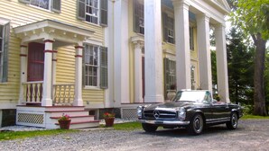 A two-story house with a porch and a parked vintage convertible.