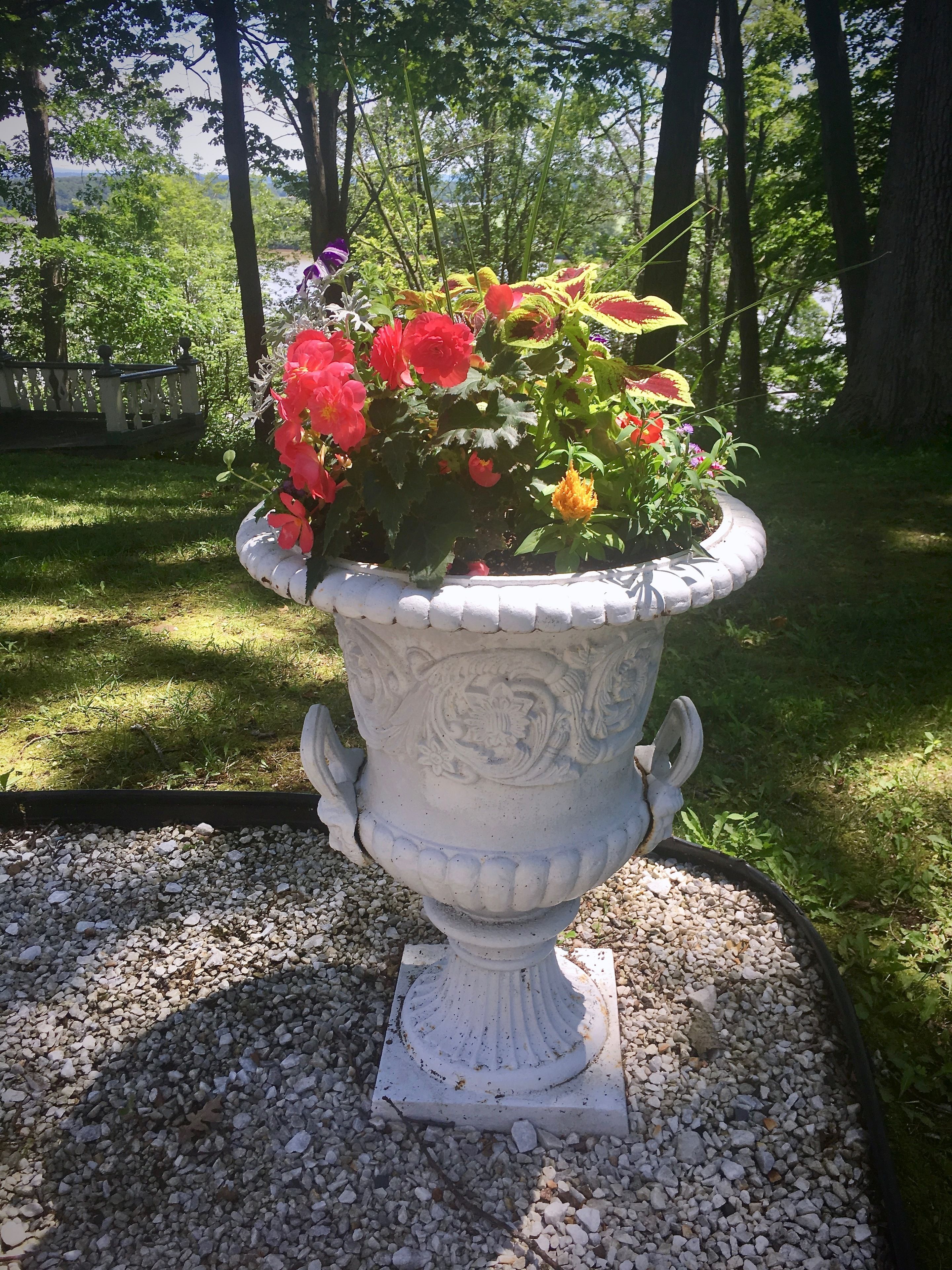 Une urne blanche ornée de motifs floraux, remplie de fleurs rouges et jaunes, posée sur du gravier.