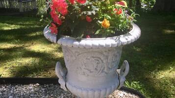 Une urne blanche ornée de motifs floraux, remplie de fleurs rouges et jaunes, posée sur du gravier.