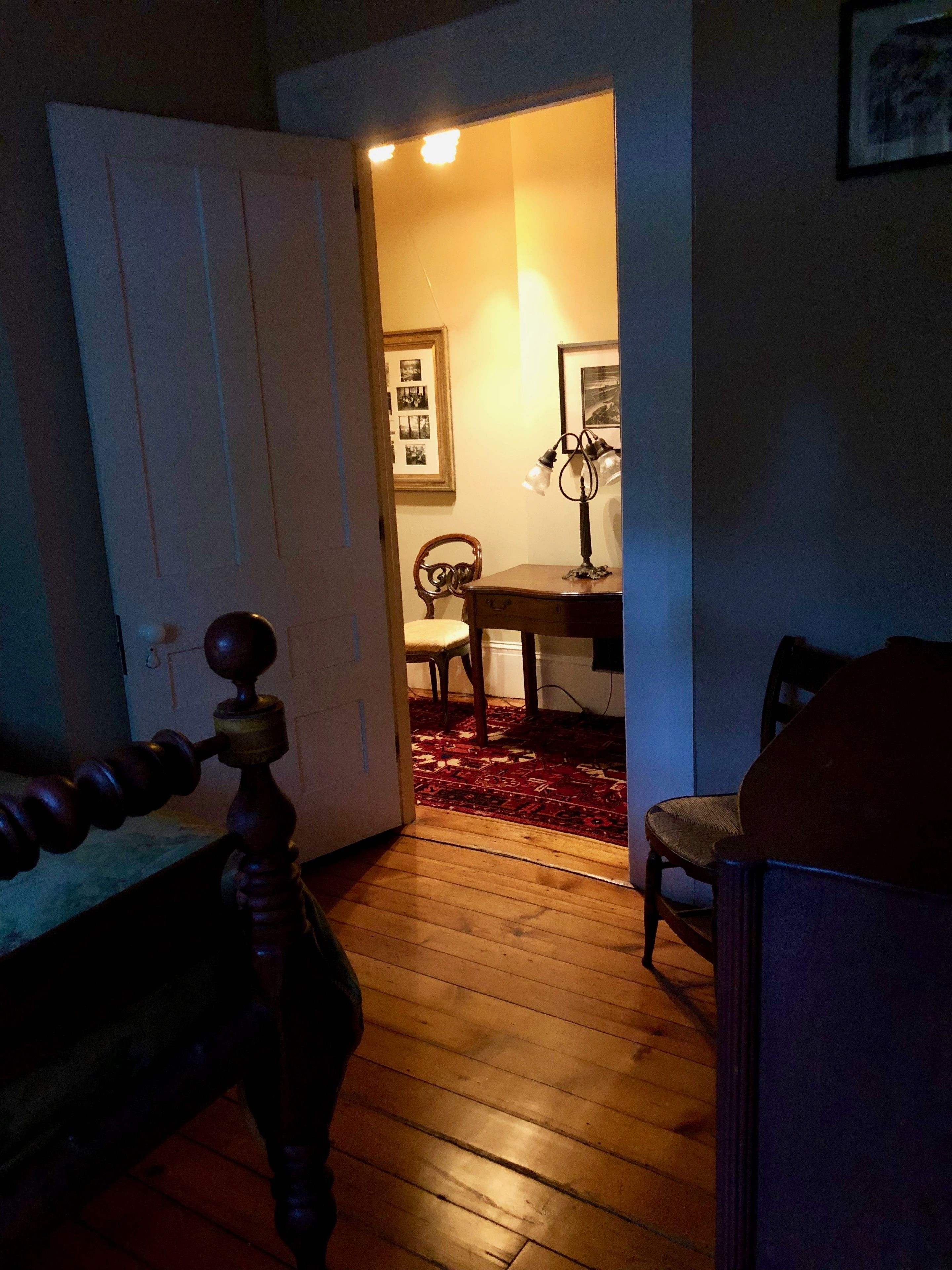 Un estrecho pasillo con suelo de madera que conduce a una habitación con una mesa y sillas para comer. Se ve una puerta a la izquierda y una lámpara a la derecha.