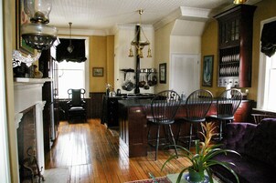A kitchen with wooden floors, a dining area with chairs, a fireplace, and a chandelier.