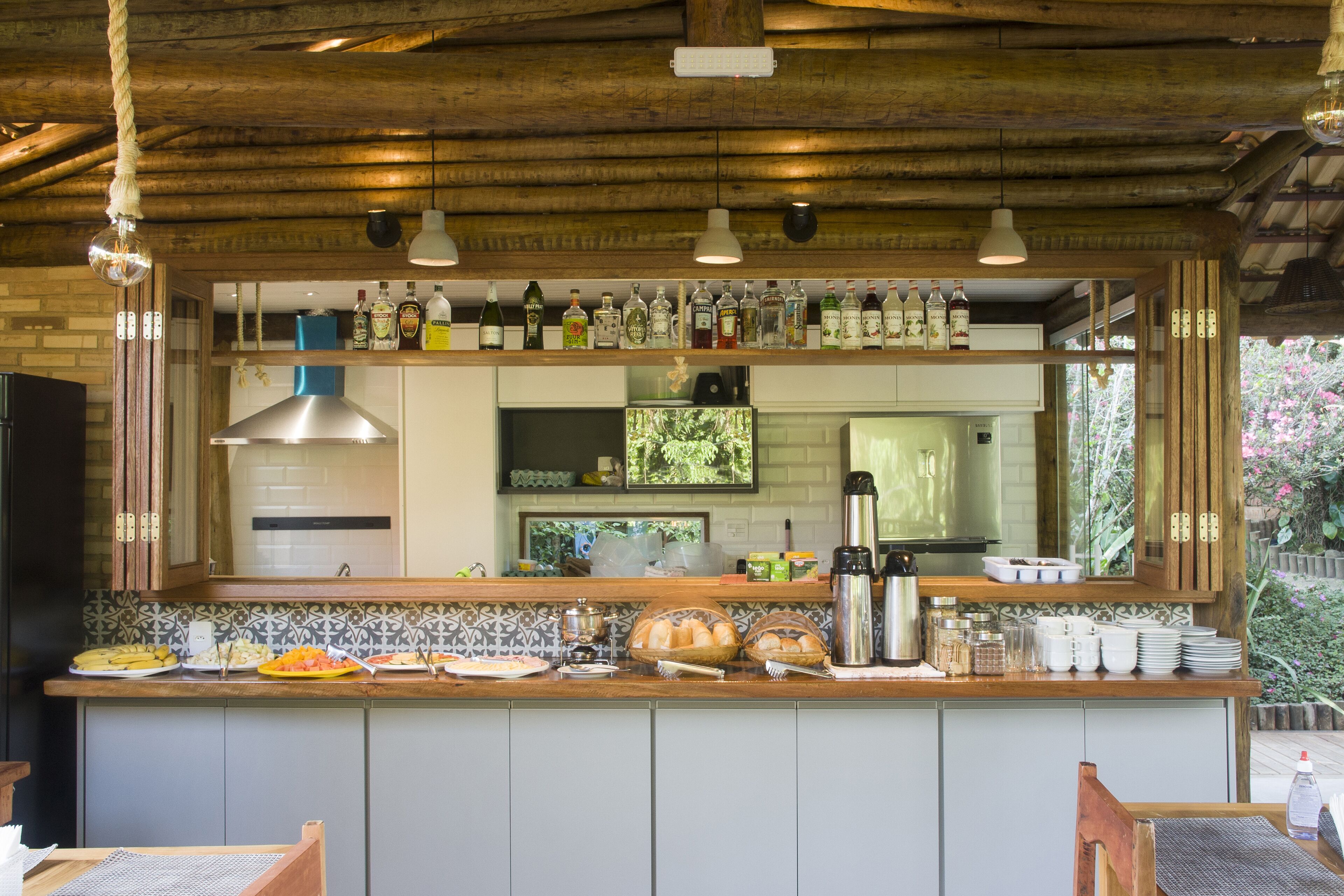 A kitchen with a wooden ceiling, a bar area with various bottles, and a view of the dining area.