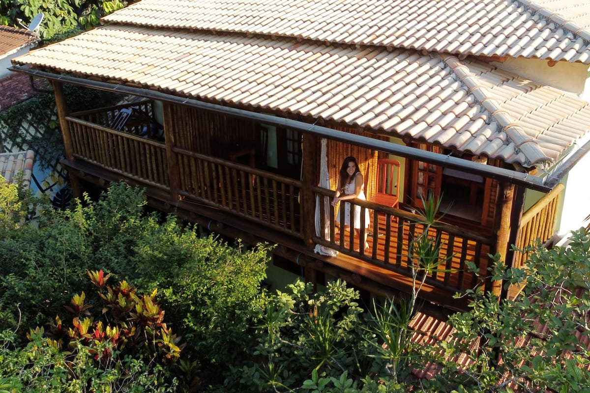 A traditional wooden house with a tiled roof, surrounded by lush greenery.