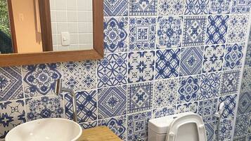 A bathroom with a white sink, wooden vanity, and a toilet with a blue and white patterned tile wall.