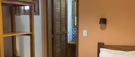 Un dormitorio con cama, una estantería de madera, un refrigerador pequeño y una puerta que da a un baño.