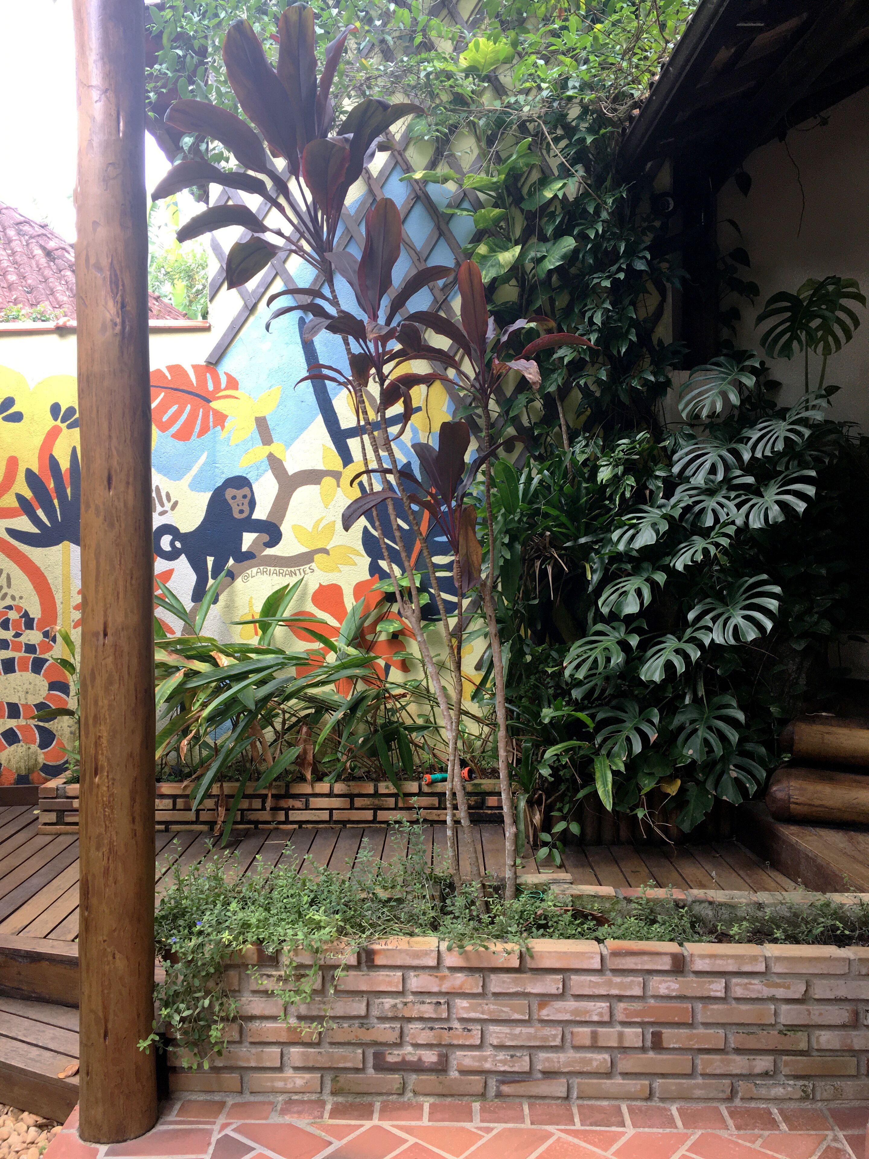 Un muro de ladrillo con un mural, un poste de madera y varias plantas.