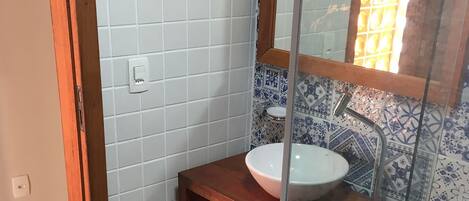 A bathroom with a white sink, a wooden vanity, a glass shower enclosure, and a tiled wall with a floral pattern.