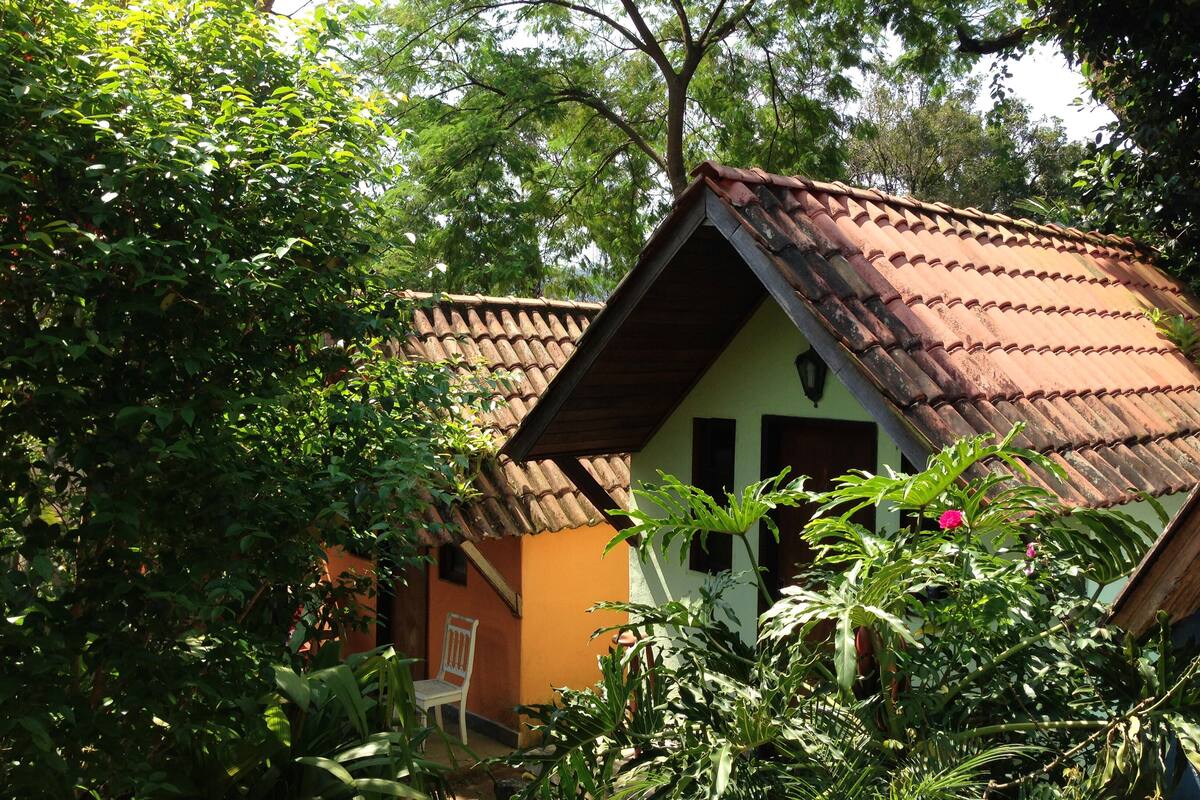 A small house with a tiled roof, surrounded by lush greenery and trees.