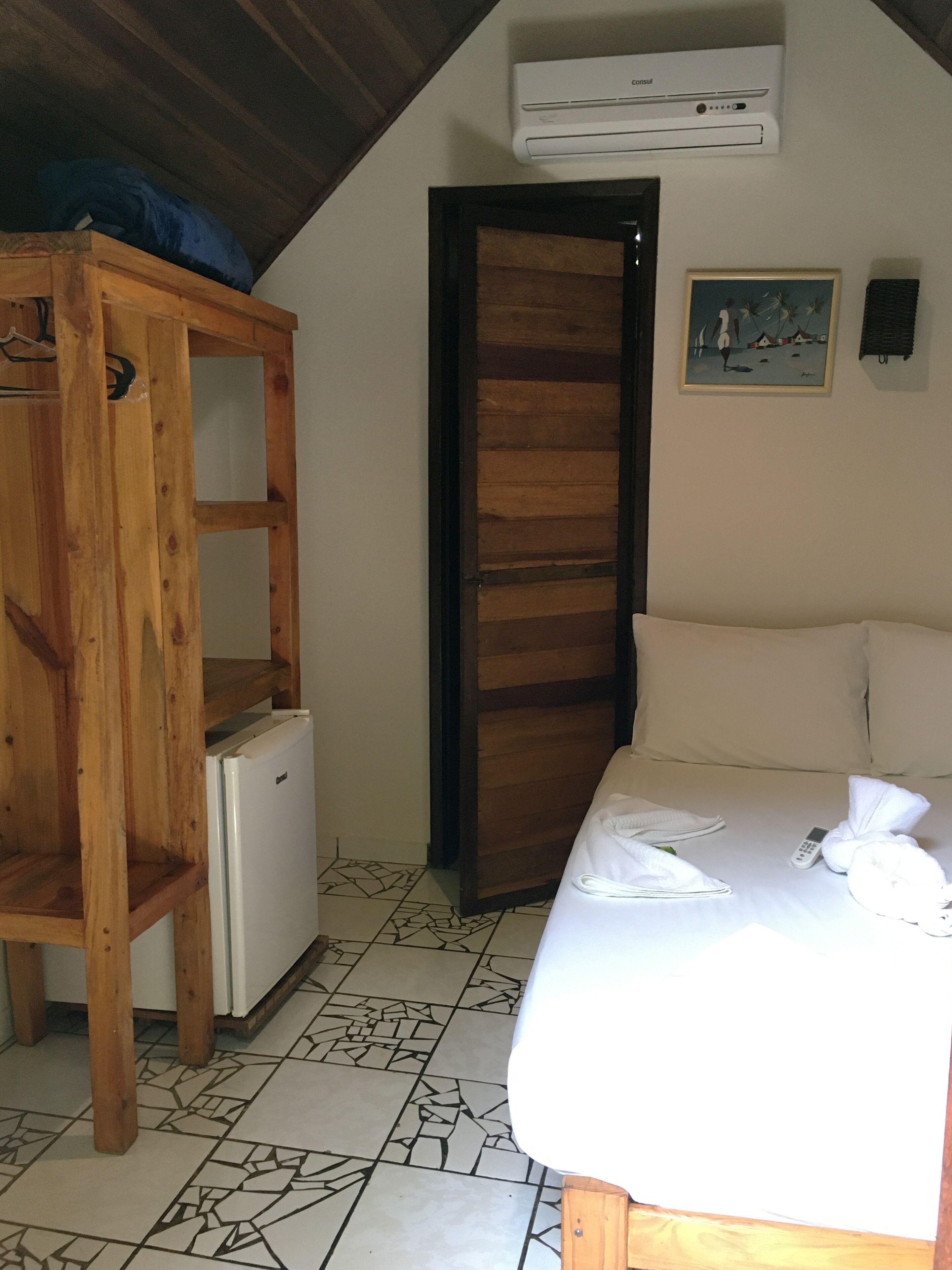 Un dormitorio con una cama, un armario de madera, un refrigerador pequeño y un equipo de aire acondicionado en la pared.