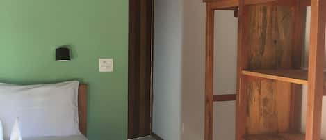 Una habitación de hotel con una cama, una mesita de noche de madera, un refrigerador blanco pequeño y una pared verde.