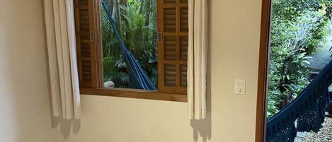 Una camera da letto con un letto, una finestra con tende, una ventola e vista su un giardino.