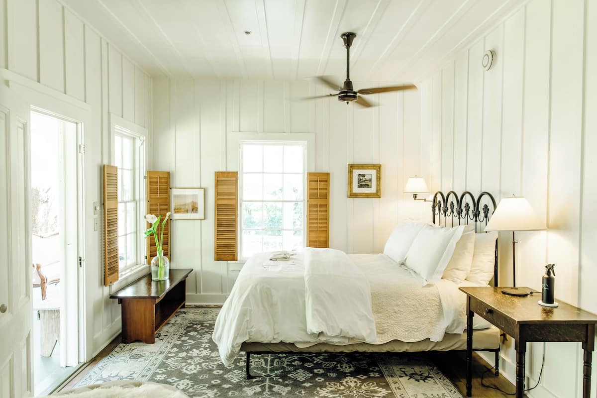 A bedroom with a bed, bedside table, lamp, and a ceiling fan.