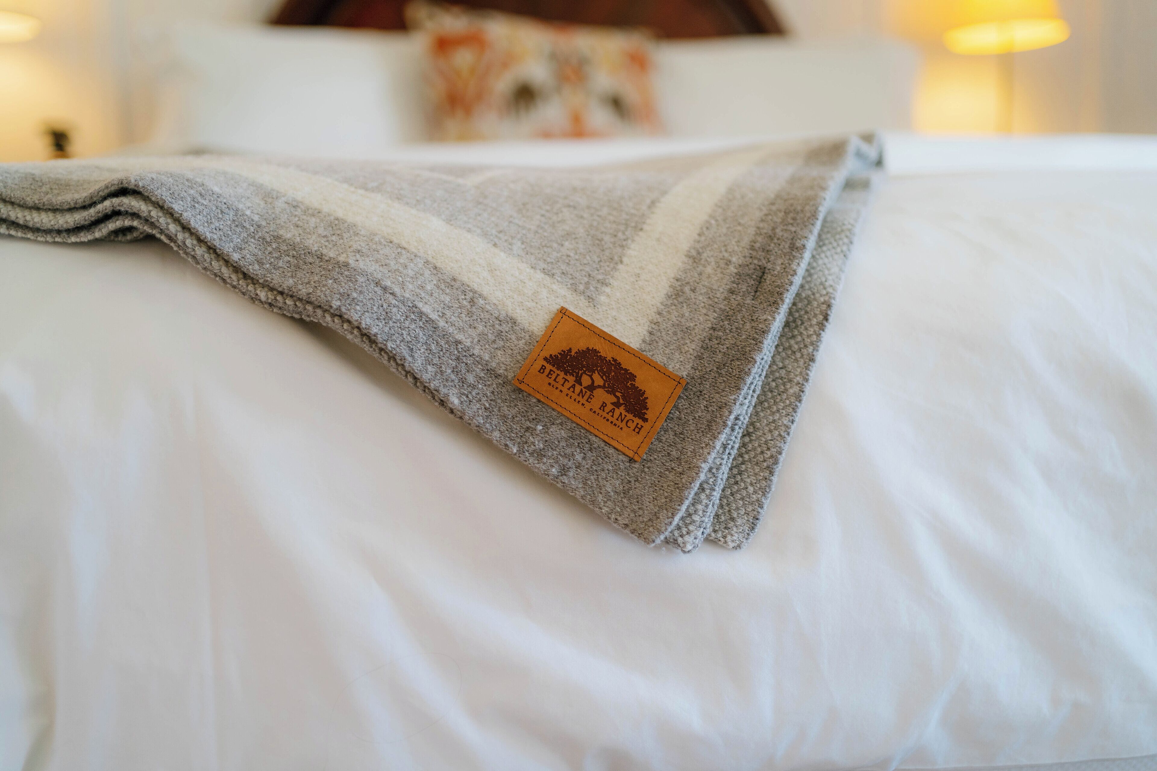 A neatly made bed with a gray and white striped blanket and a brown tag.