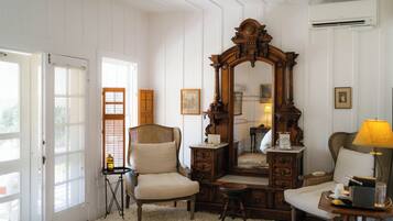 Una habitación con un espejo grande, una silla, una mesa con lámpara y un taburete pequeño.