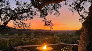Une vue sur le coucher de soleil depuis une terrasse, avec deux fauteuils Adirondack placés face à un foyer extérieur.