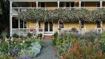 Una casa de dos pisos con un porche cubierto y un jardín con diversas flores.