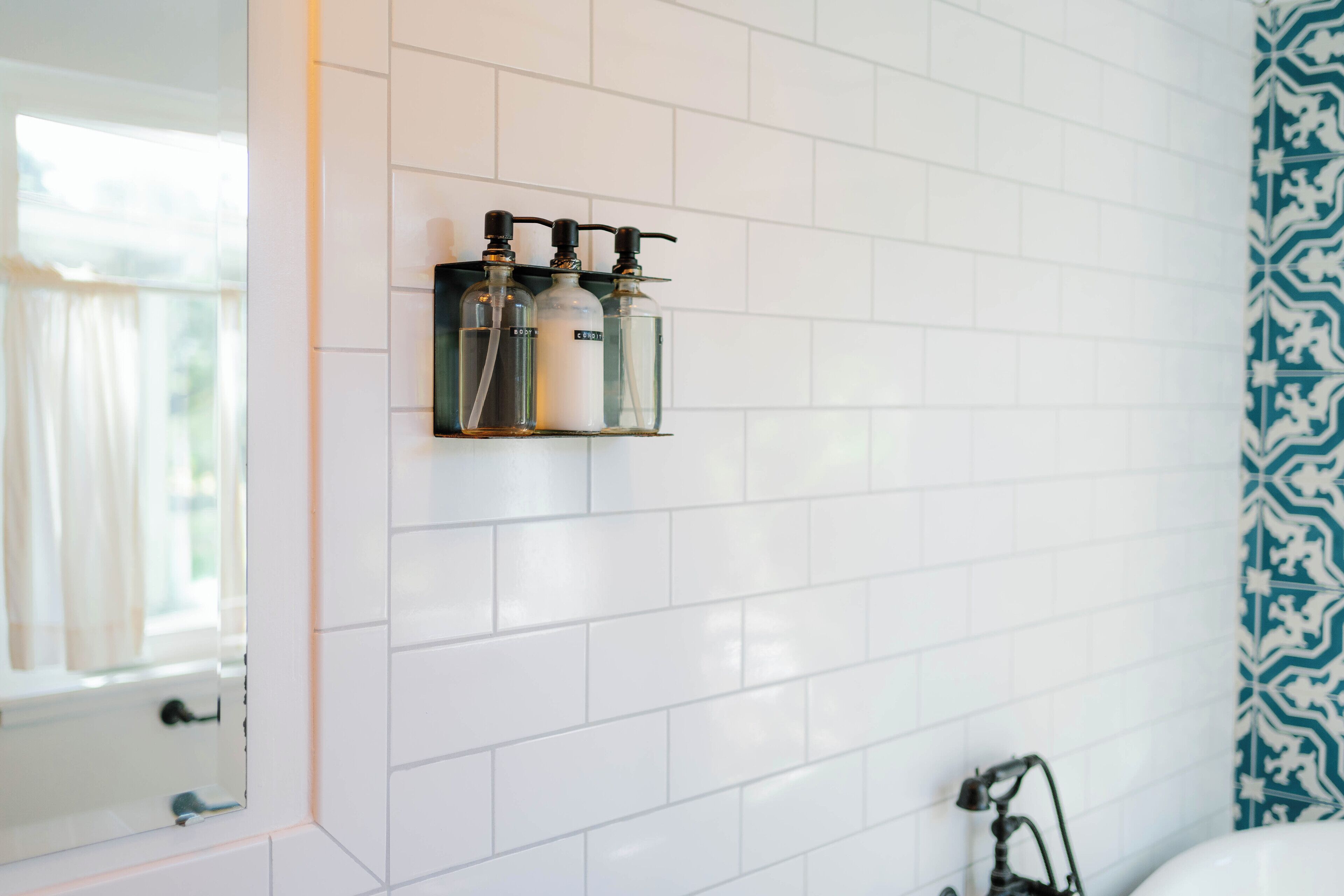 A bathroom with white tiled walls, a window with curtains, and a patterned shower curtain.
