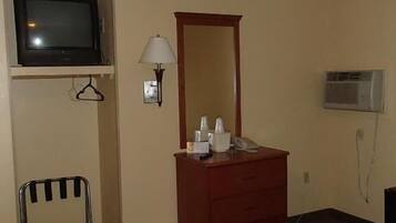 A hotel room with a bed, a dresser, a television, a mirror, a lamp, and an air conditioning unit.
