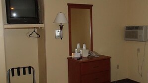 A hotel room with a TV, a mirror, a lamp, a vanity with toiletries, a chair, and an air conditioning unit. - Royal Inn of New Orleans (New Orleans)