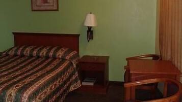 A hotel room with a bed, a nightstand, a lamp, a chair, and a picture on the wall.