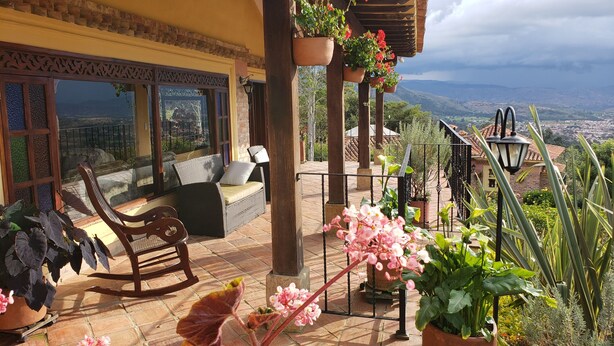 A terrace with wicker furniture, potted plants, and a view of the city. - Hotel La Primavera Suites & Casas Campestres (Villa de Leyva)