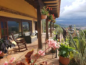 A terrace with wicker furniture, potted plants, and a view of the city. - Hotel La Primavera Suites & Casas Campestres (Villa de Leyva)