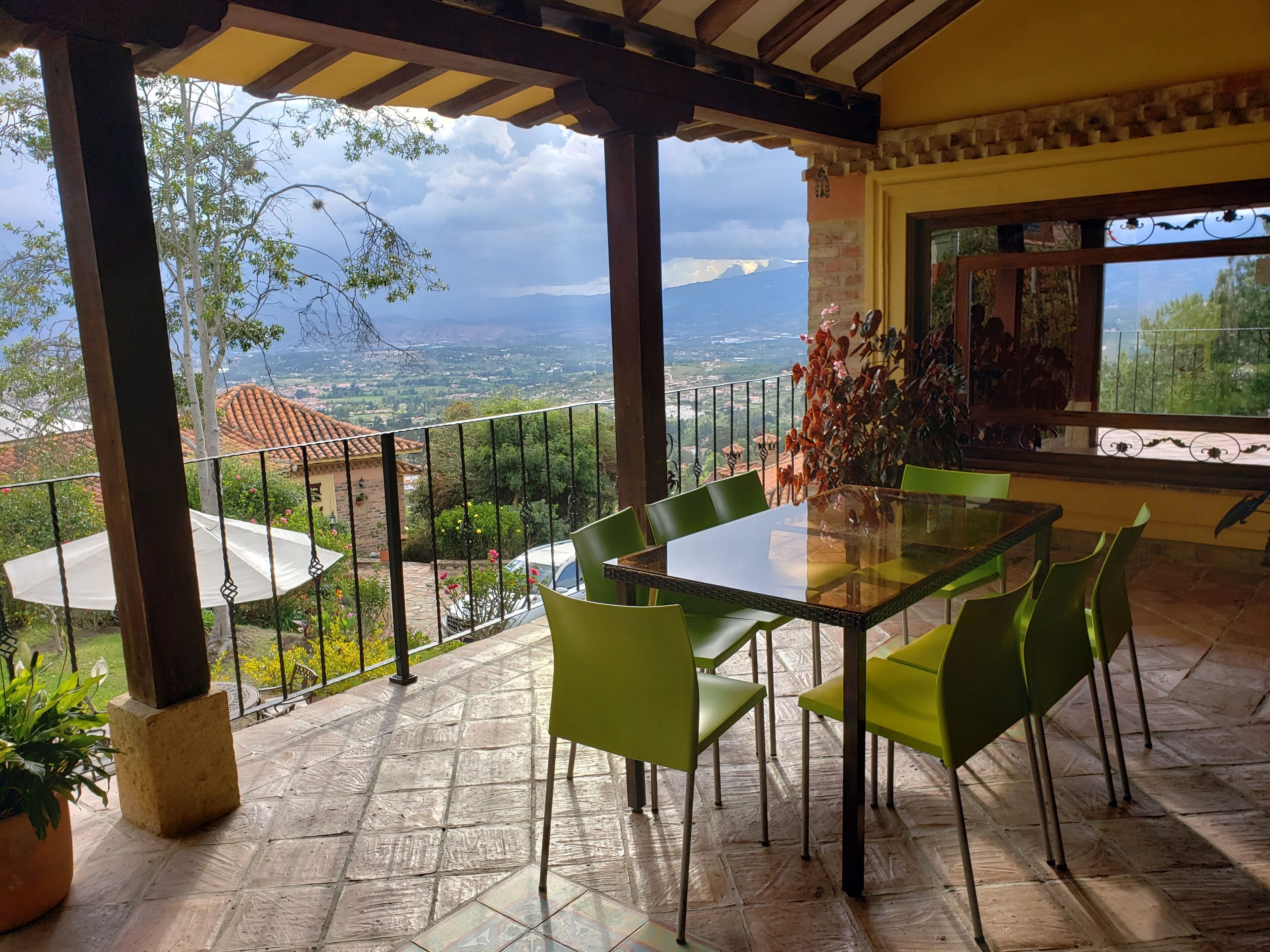 Un patio cubierto con una mesa y sillas, vista al campo y barandilla de balcón.
