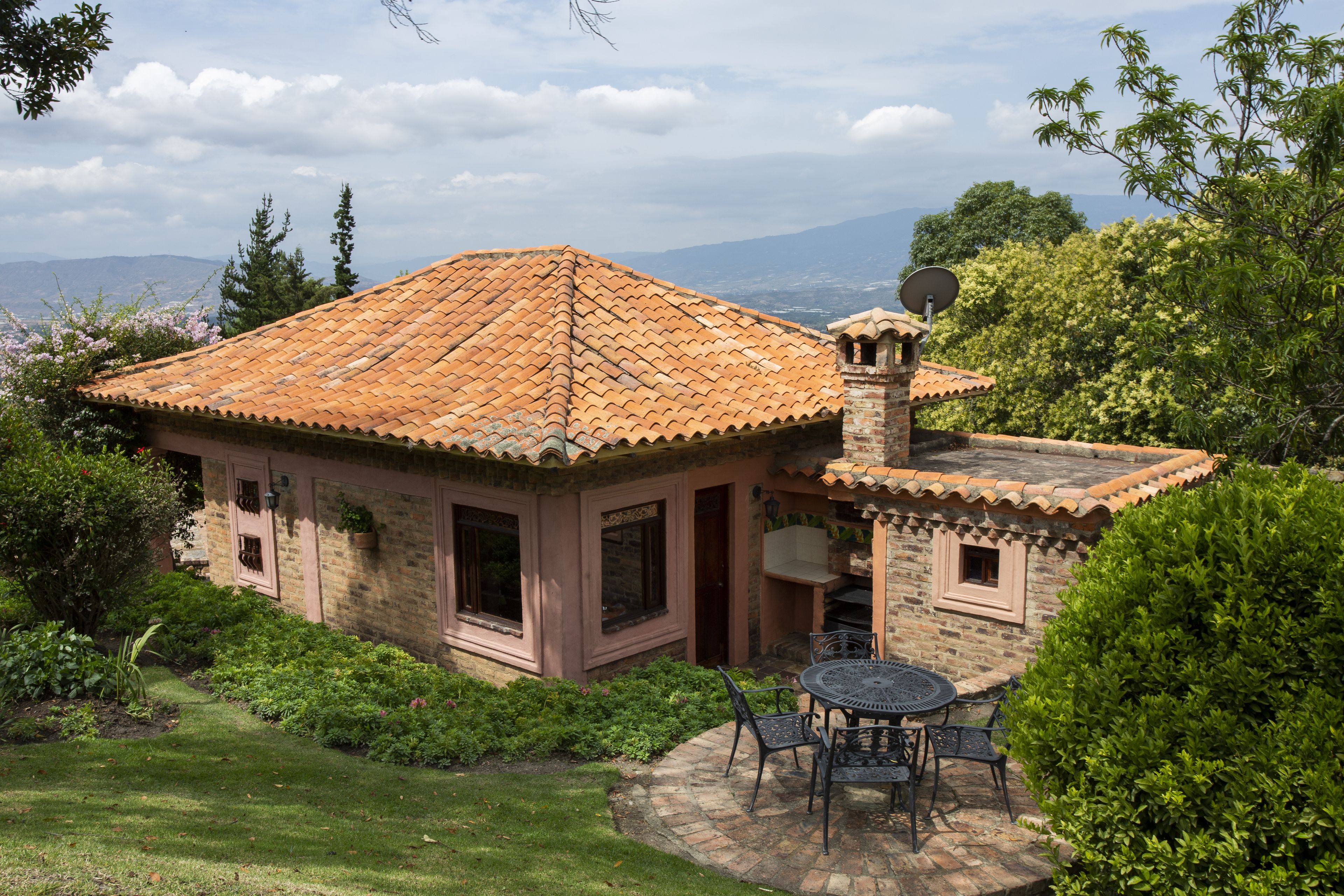 Una casa de piedra con techo de tejas, un patio con mesa y sillas, y una antena parabólica.