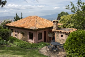 A stone house with a tiled roof, a patio with a table and chairs, and a satellite dish.