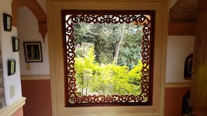 A room with a large ornate window, framed by a decorative wooden border, leading to a garden with lush greenery. - Hotel La Primavera Suites & Casas Campestres (Villa de Leyva)