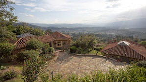 A stone courtyard with tiled-roof buildings, surrounded by lush greenery and offering a panoramic view of distant mountains and valleys. - Hotel La Primavera Suites & Casas Campestres (Villa de Leyva)