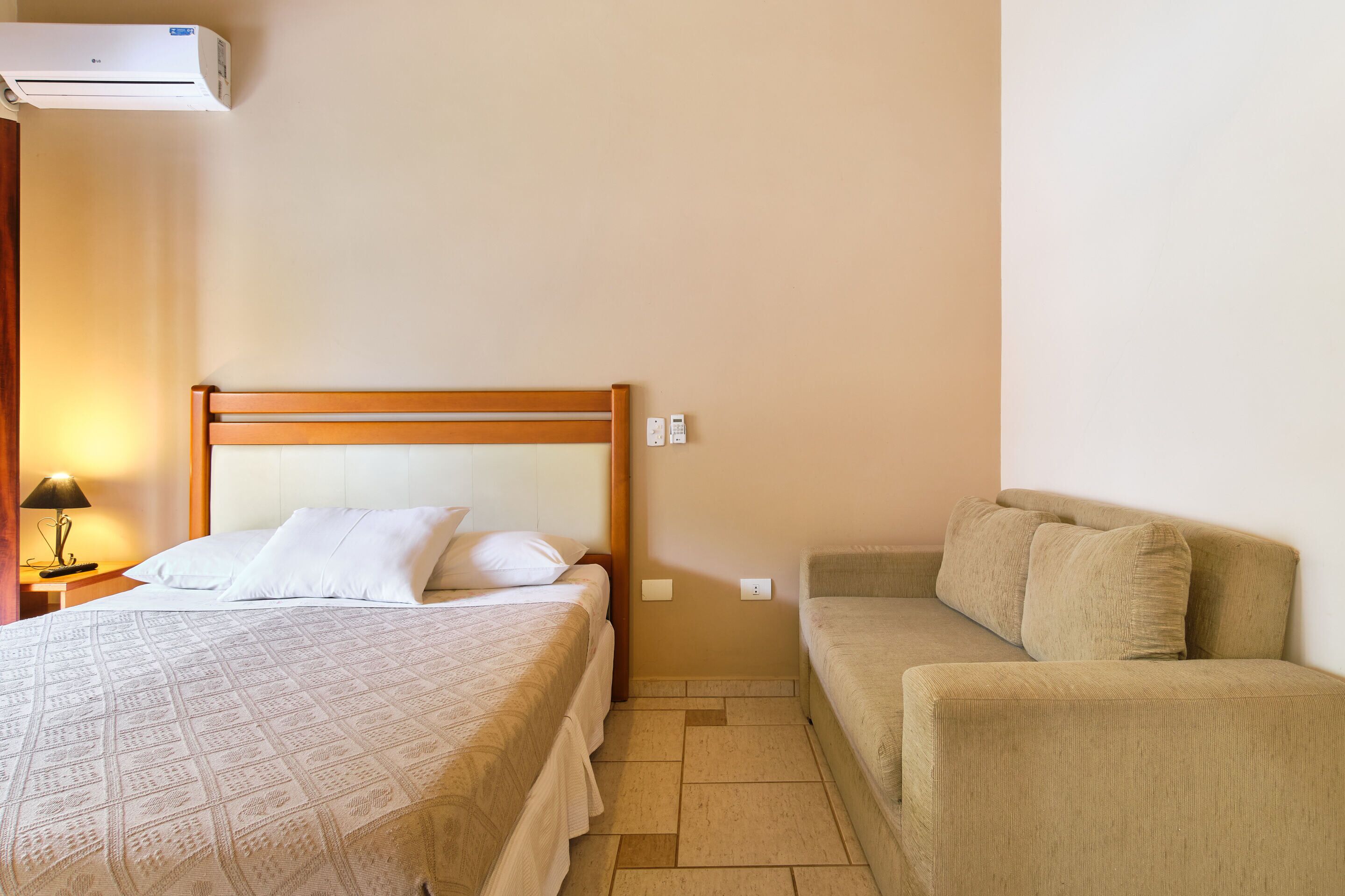 Ein Schlafzimmer mit einem Bett, einem Nachttisch mit Lampe, einem Sofa und einer Klimaanlage.